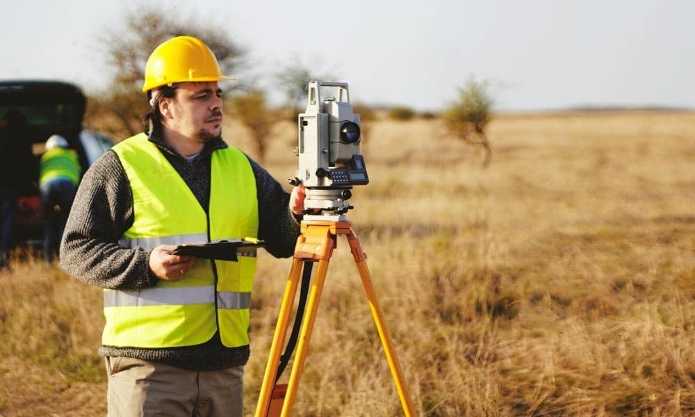 Land surveyor performing a property survey with a total station in an open field