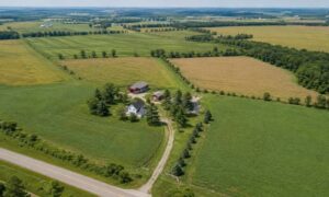 Aerial view of a large farmland property with multiple fields, farm buildings, and a private access road