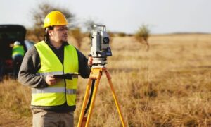 Land surveyor performing a property survey with a total station in an open field